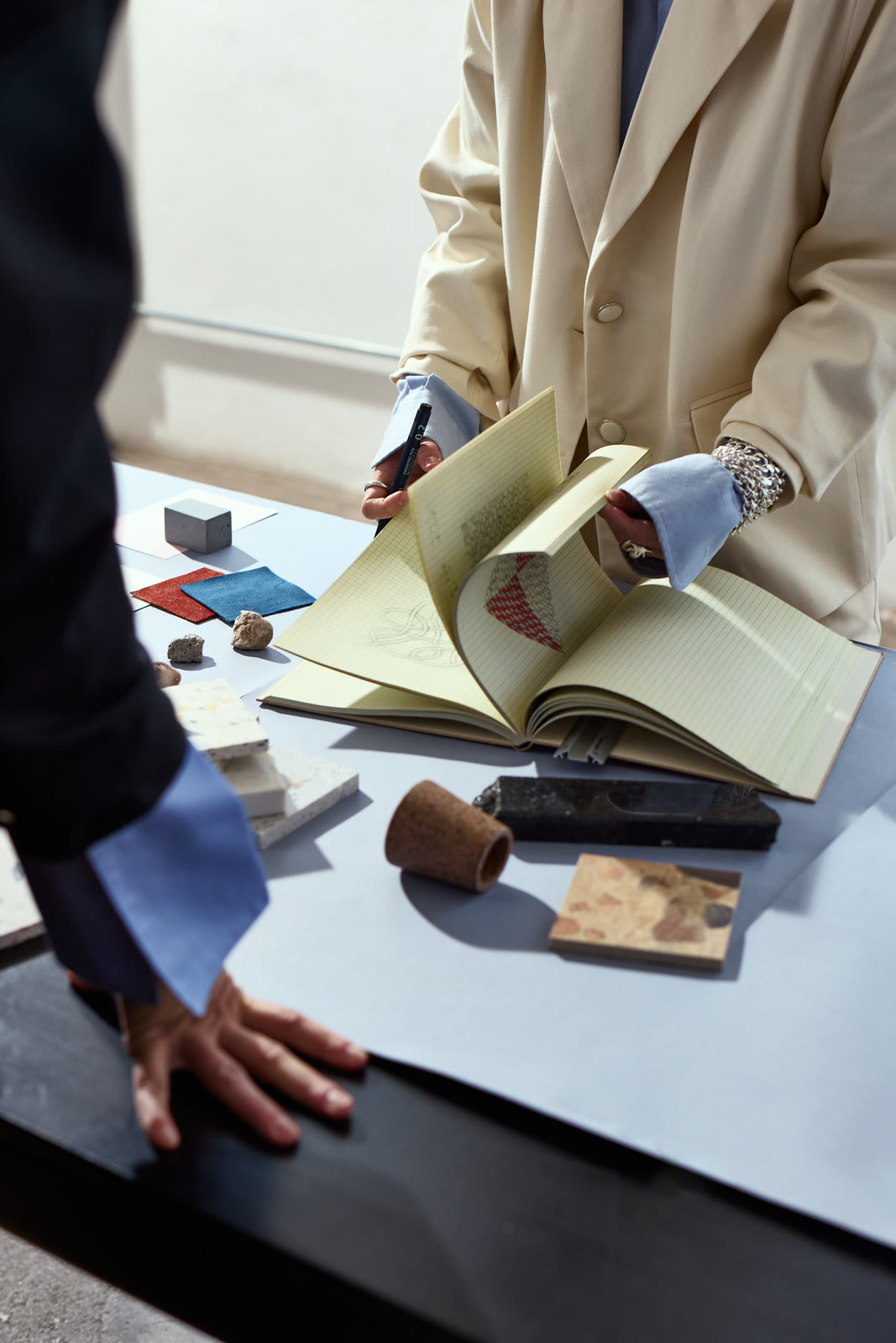 Hands reviewing material samples and a notebook on a studio desk